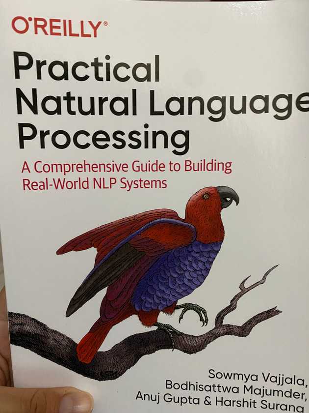 Libro títulado en inglés Practical Natural Language Processing, de portada tienen un pájaro parecido a un cotorro de color rojo con la panza púrpura parado en una pata sobre una rama